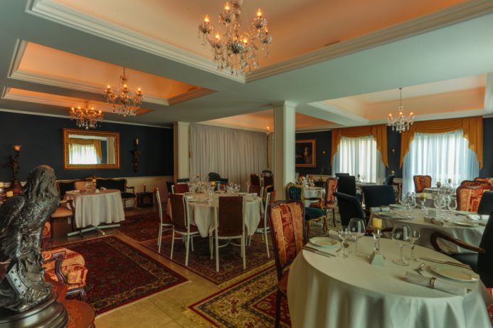 Interior do Restaurante Cordon Blanc com mesas redondas, cadeiras almofadadas e lustres elegantes.